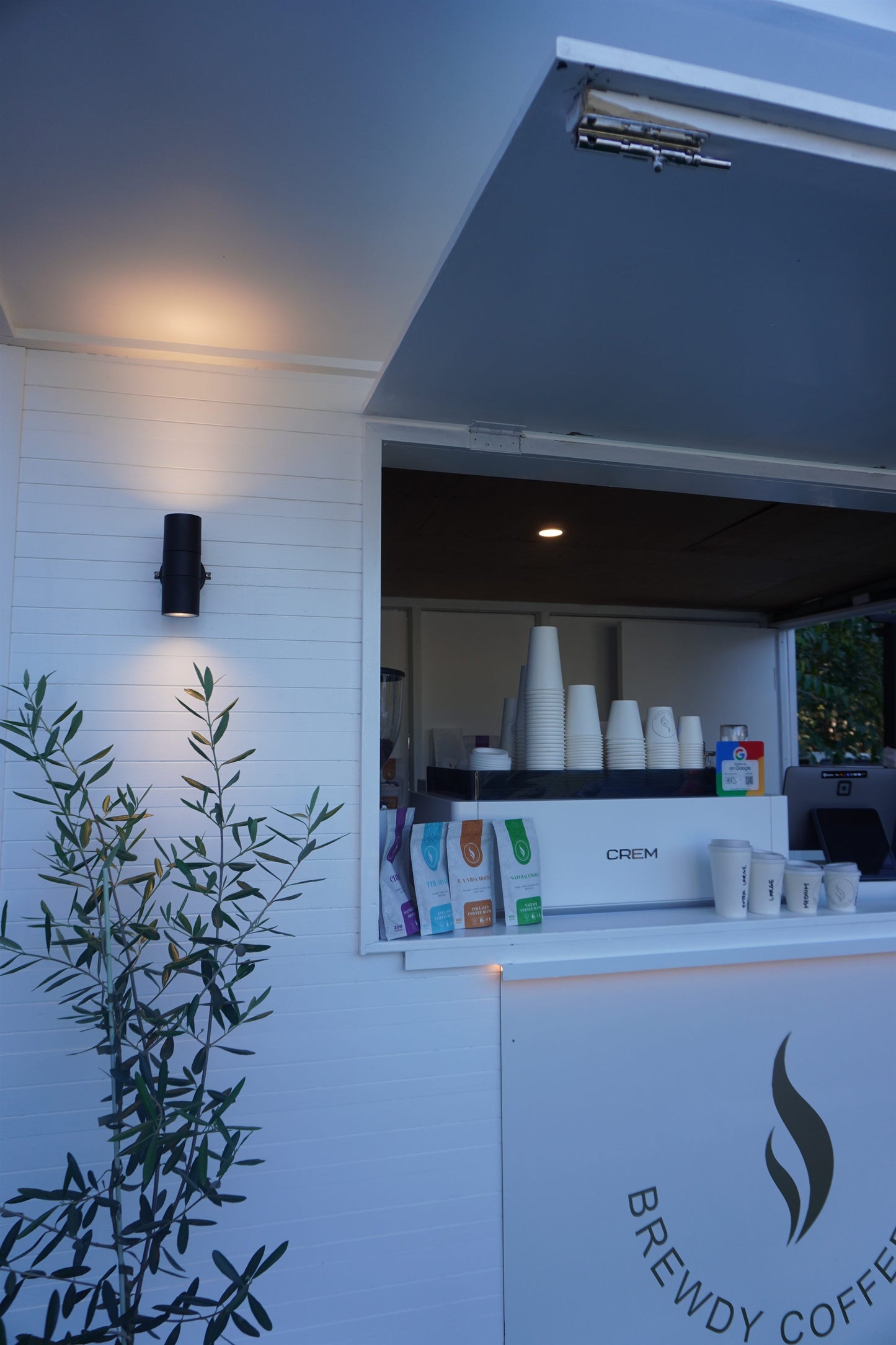 The Brewdy coffee kiosk glowing at dusk with the range in the window