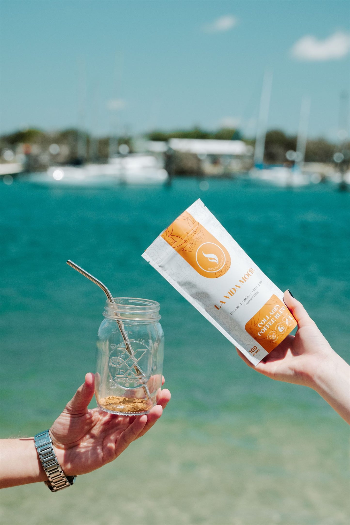 Hands holding a jar of iced coffee and a Brewdy pouch over turquoise water